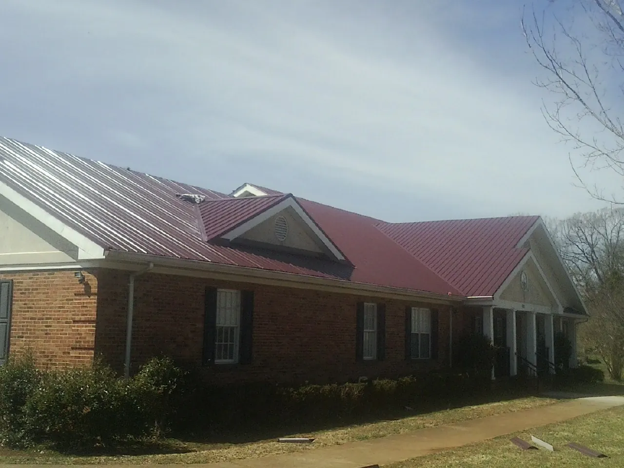 Red metal roof with gabled entries on a long brick building, from a Hail Damage Roof Repair job in Osceola Mills