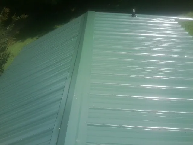 New green metal panels meeting at the ridge of a roof — Flat Roof Repair work by our crew in Osceola Mills
