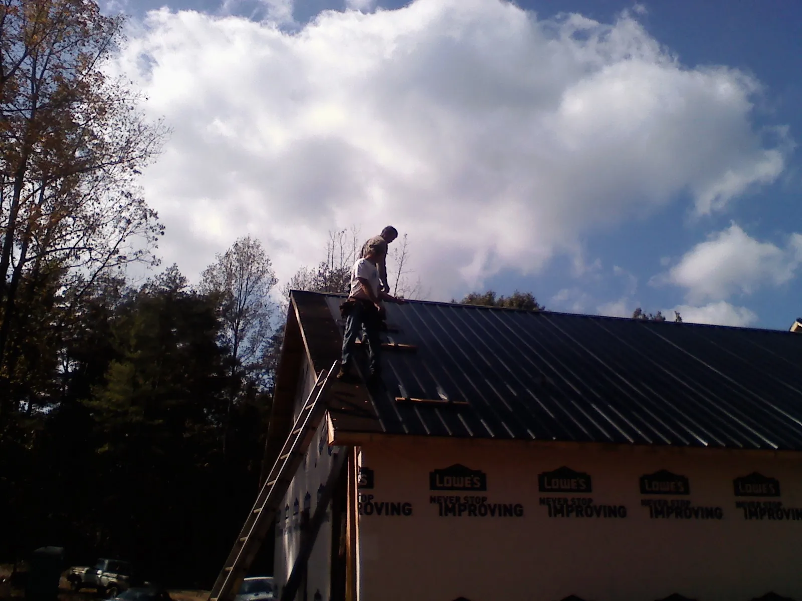 Roofer fastening dark metal panels high against a cloudy sky, from a Roof Inspection job in Osceola Mills