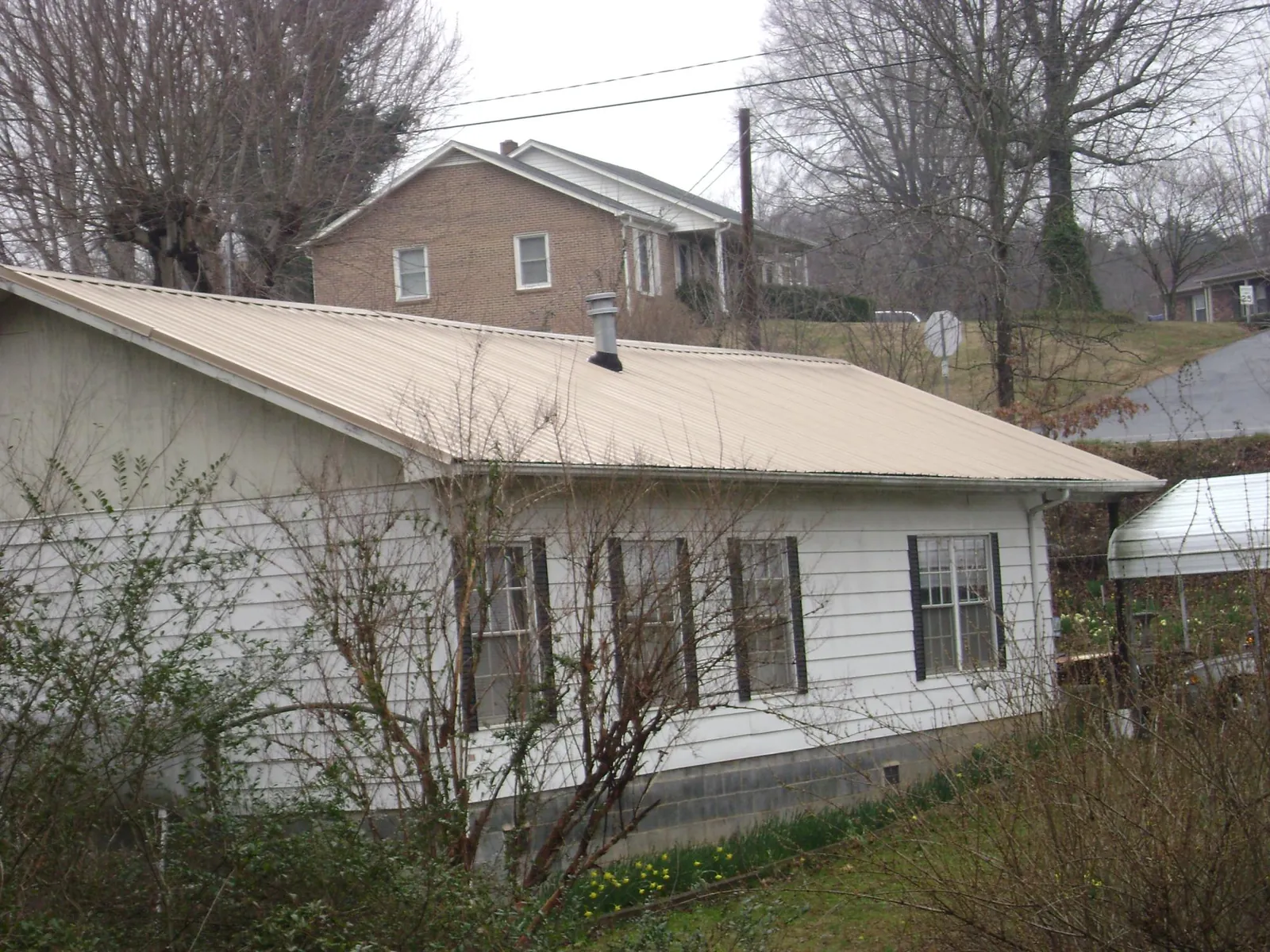 Tan metal roof on a white sided house set into a hillside — Commercial Roofing by Roofing Brothers in Osceola Mills